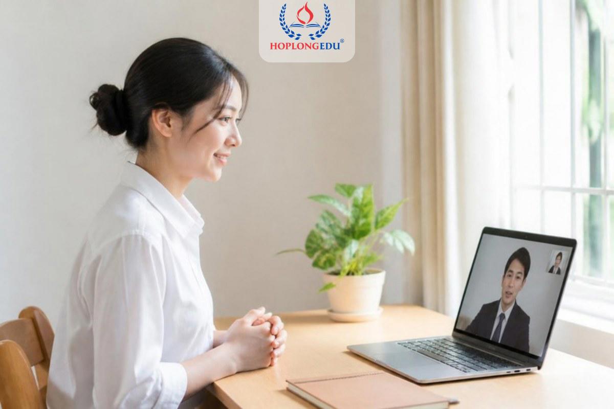 Học sinh mặc áo sơ mi trắng ngồi thẳng, mỉm cười khi phỏng vấn online với trường Hàn Quốc qua laptop