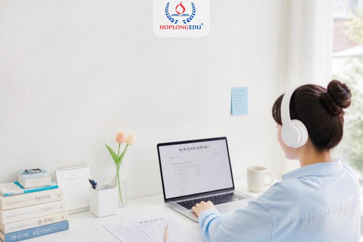Học viên đeo tai nghe làm đề thi TOPIK trên máy tính, bên cạnh là phiếu trả lời