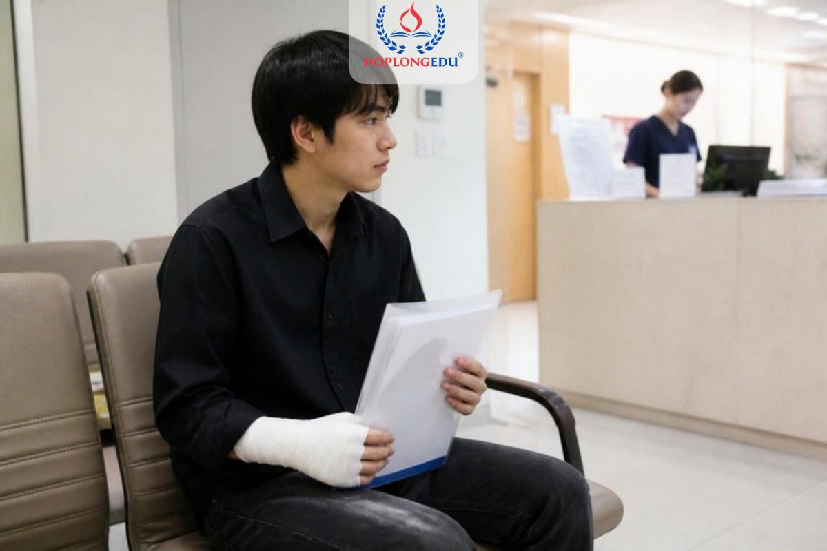 Du học sinh Việt Nam bị thương ở tay ngồi chờ khám tại phòng khám ở Hàn Quốc, tay cầm giấy tờ