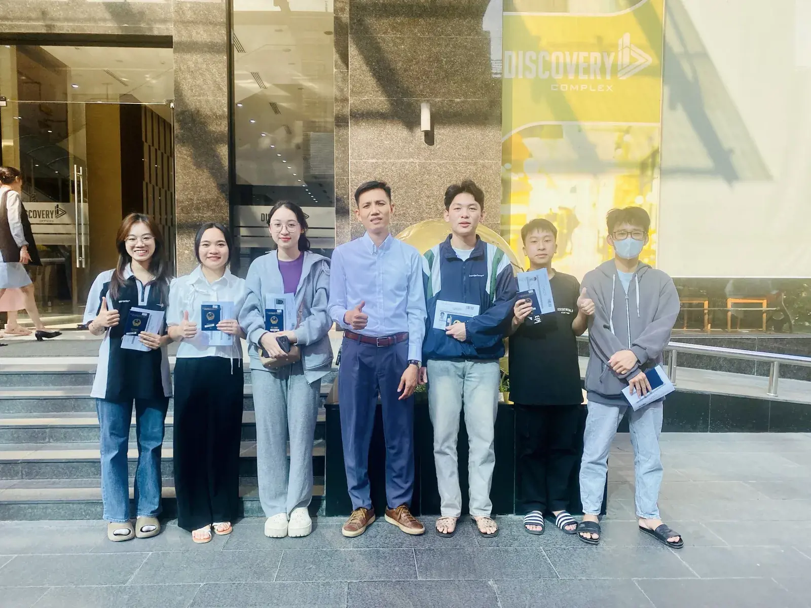 Sáu học viên Hợp Long cầm hộ chiếu có visa du học Hàn Quốc chụp cùng giám đốc trước tòa nhà Discovery Complex