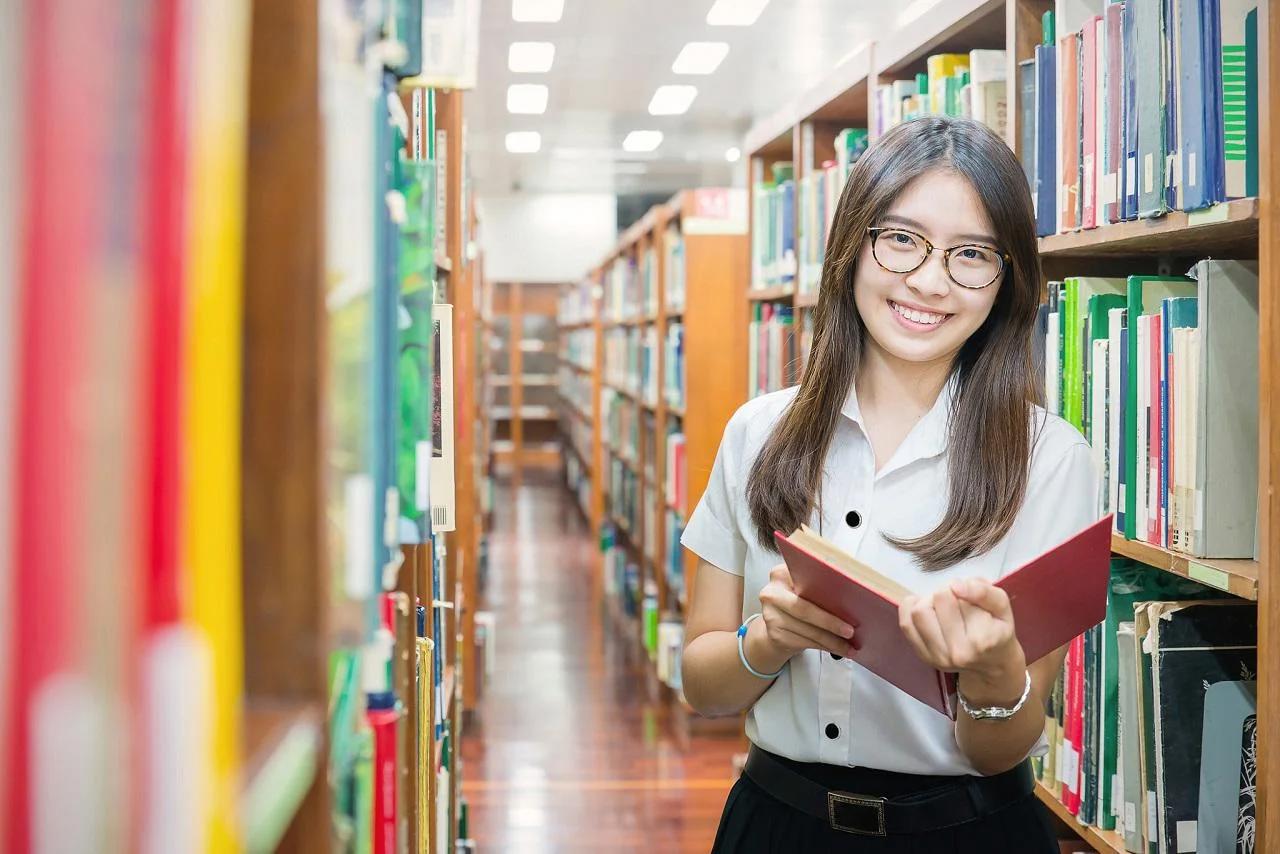 Nữ sinh cầm sách đứng giữa hai dãy kệ trong thư viện