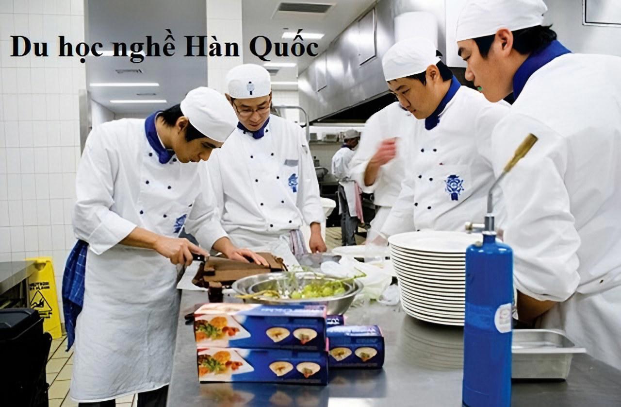 Nhóm đầu bếp mặc đồng phục trắng đang chuẩn bị món ăn trong bếp công nghiệp