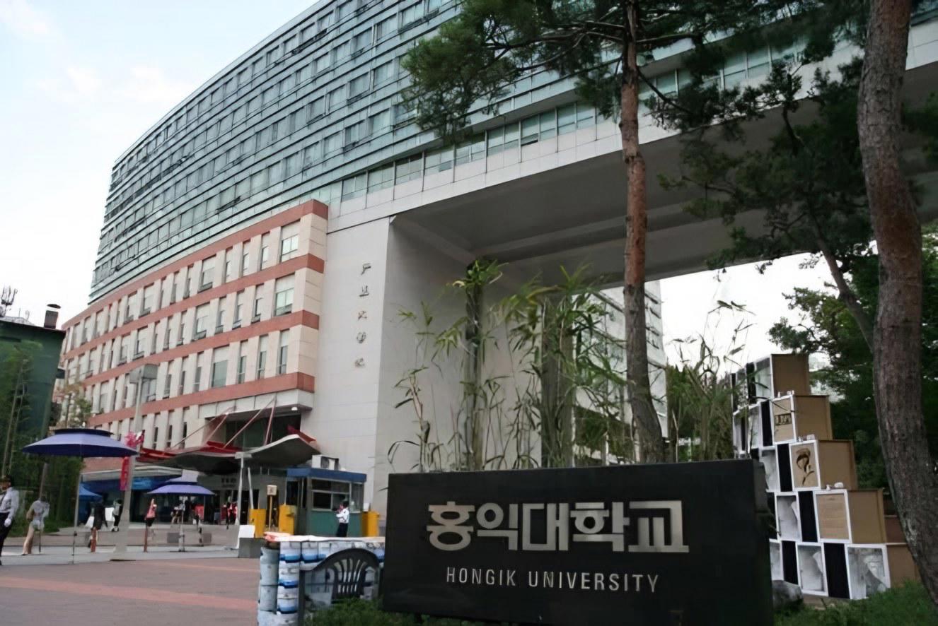 Cổng chính Đại học Hongik với tấm đá khắc tên trường bằng tiếng Hàn và tiếng Anh, phía sau là toà nhà học